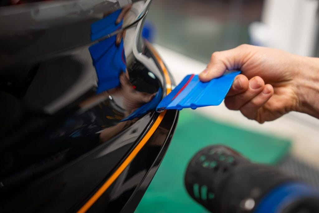 A worker smooths vinyl wrap on a car bumper